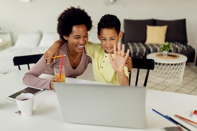 Heureuse mère et fils afro-américains ayant un appel vidéo sur un ordinateur portable à la maison