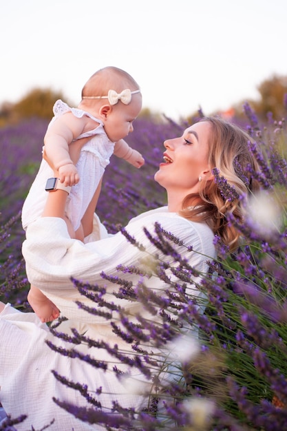 Heureuse mère avec jolie fille sur fond de lavande. Belle femme et mignon bébé assis en m