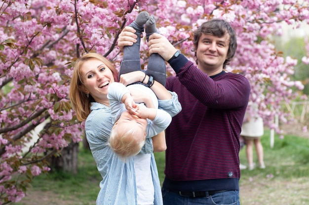 Heureuse mère père et petit garçon fils s'amusant dans le parc du printemps près de l'arbre en fleurs de sakura rose Concept de printemps