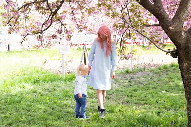 Heureuse mère avec petit fils dans le parc à pied près de l'arbre de sakura