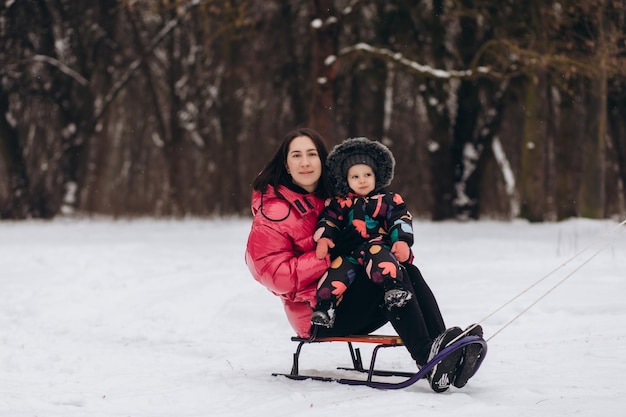 Heureuse mère avec une petite fille assise sur un traîneau et faisant de la luge sur la neige depuis la colline