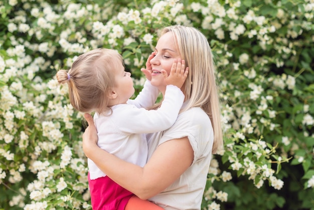 Heureuse mère et petite fille dans le parc par une journée ensoleillée au coucher du soleil Maman et enfant en plein air Concept de tendresse famille mère célibataire fleurs sourires câlins santé mentale harmonie