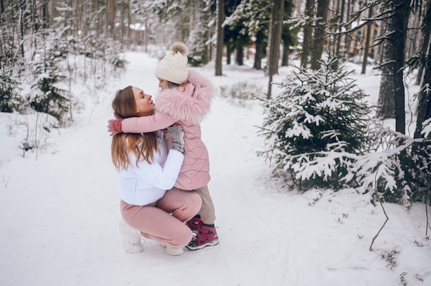 Heureuse Mère Et Petite Fille Mignonne En Vêtements Chauds Roses Marchant S'amusant Et Serrant Dans La Forêt De Conifères D'hiver Froid Blanc Neigeux Avec Bois D'épinettes à L'extérieur