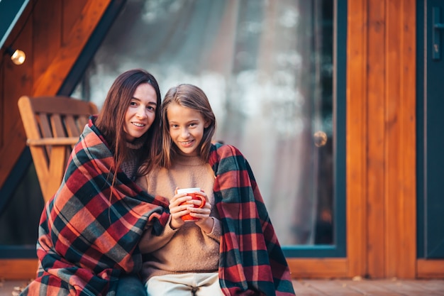 Heureuse mère et petite fille avec mug au jour d'automne enveloppé dans une couverture à l'extérieur