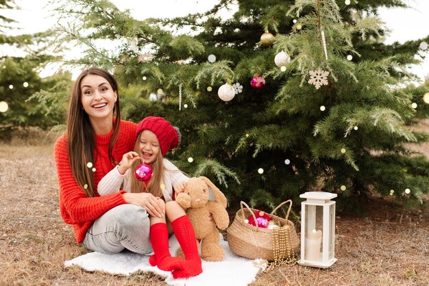 Heureuse mère avec petite fille porter des pulls en tricot rouge décorer l'arbre de Noël à l'extérieur