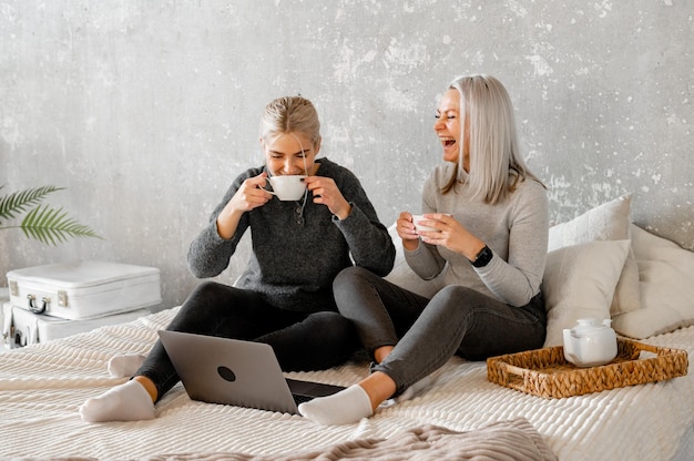 Heureuse mère avec une petite fille s'amusant en ligne avec une application regardant des dessins animés vidéo ou jouant à un jeu sur un ordinateur portable ensemble jeune baby-sitter ou nounou apprenant à une fille à utiliser un ordinateur