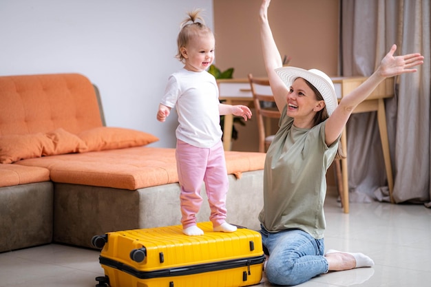 Heureuse mère et petite fille avec valise jaune bagages et famille de vêtements prêts à voyager en vacances à la maison