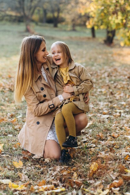 Heureuse mère et sa belle fille assise et s'amusant parmi les feuilles jaunes dans le parc en automne.