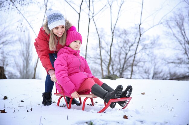 Heureuse mère avec sa fille faisant de la luge dans un parc enneigé en vacances d'hiver