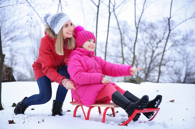 Heureuse mère avec sa fille faisant de la luge dans un parc enneigé en vacances d'hiver