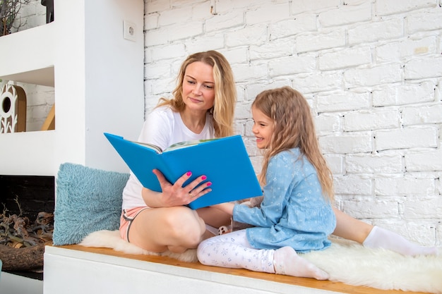 Heureuse mère avec sa fille lisant un livre et souriante assise par terre dans le salon