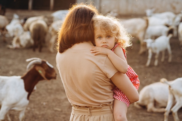 Heureuse mère et sa fille passent du temps dans une ferme écologique parmi les chèvres.