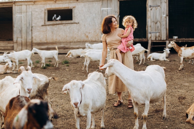 Heureuse mère et sa fille passent du temps dans une ferme écologique parmi les chèvres.