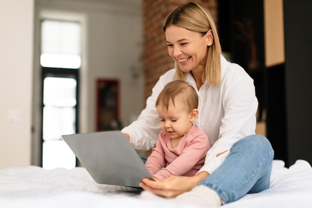 Heureuse mère et sa petite fille à l'aide d'un ordinateur portable à la maison femme montrant des dessins animés à un enfant en bas âge