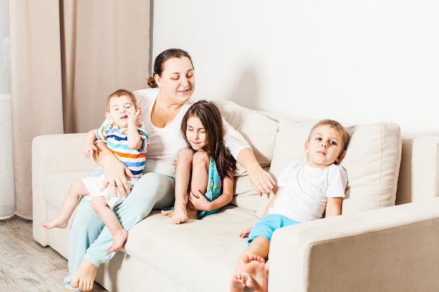 Heureuse mère avec ses petits enfants à la maison. Belle jeune femme veut embrasser ses enfants.