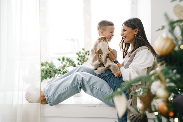 Heureuse mère avec son fils s'asseoir sur le rebord de la fenêtre près de l'arbre de Noël