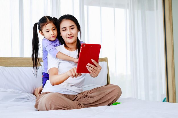 Heureuse mère souriante et petite fille faisant un selfie et un appel vidéo technologique ensemble à la maison