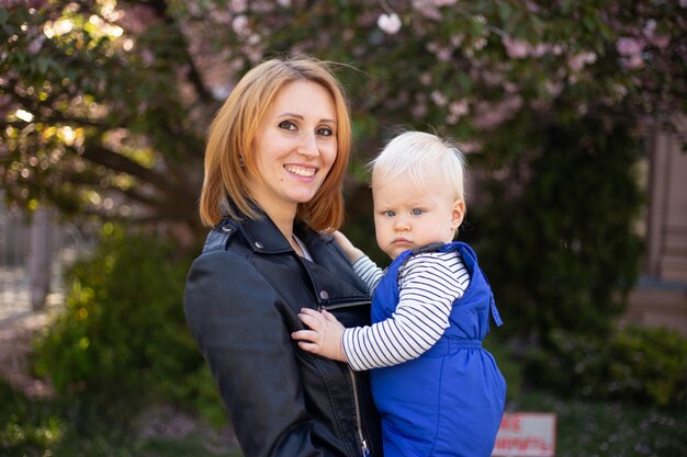 Heureuse mère tient dans ses bras un petit fils mignon Maman et petit garçon dans un jardin fleuri Sakura