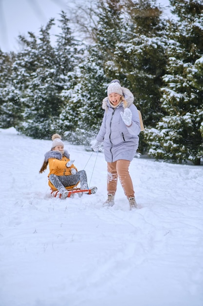 Heureuse mère tirant un traîneau avec une petite fille sur la route du parc enneigé