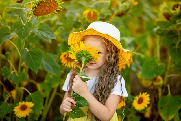 heureuse petite belle fille renifle un tournesol dans un champ en été.