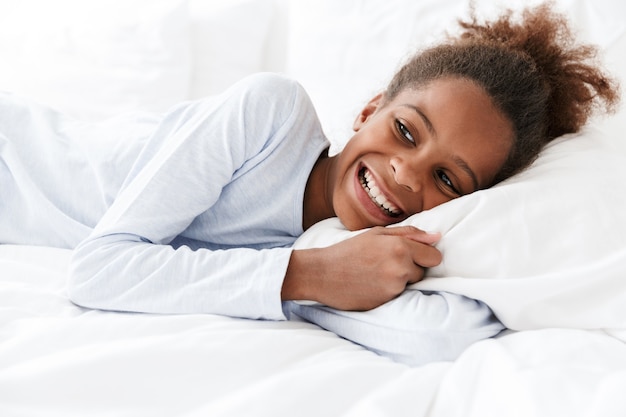 heureuse petite fille afro-américaine souriante et allongée dans son lit à la maison