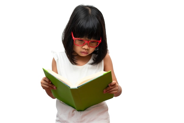 Heureuse petite fille d'âge préscolaire asiatique portant des lunettes rouges tenant et lisant un livre vert sur fond blanc isolé. Concept d'écolier et d'éducation à l'école élémentaire et préscolaire, école à domicile