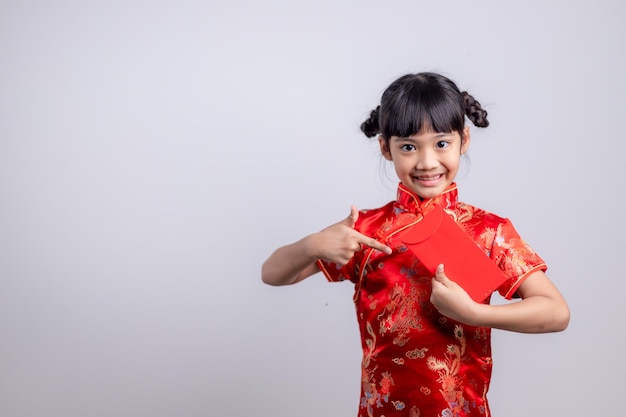 Heureuse petite fille asiatique en costume traditionnel chinois souriant et tenant une enveloppe rouge. Concept de joyeux nouvel an chinois.