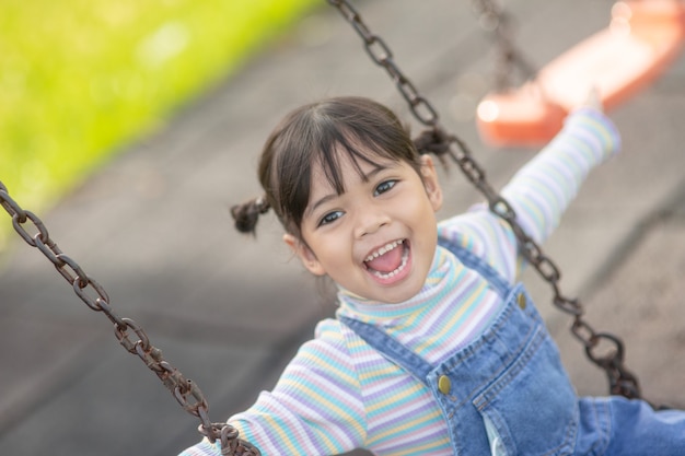 Heureuse petite fille asiatique jouant à la balançoire en plein air dans le parc