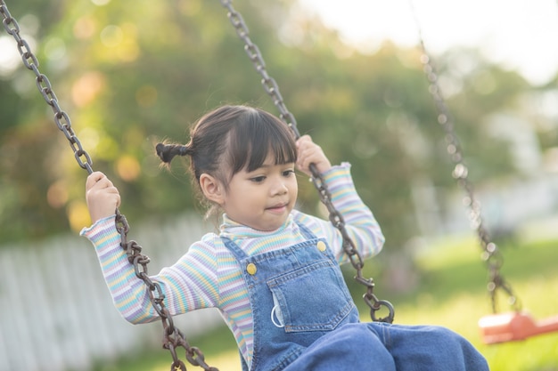 Heureuse petite fille asiatique jouant à la balançoire en plein air dans le parc