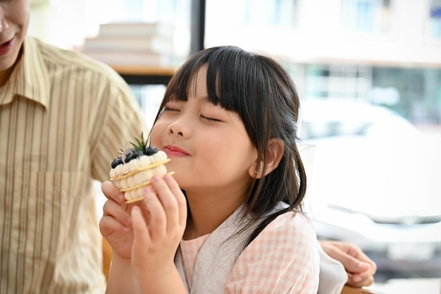 Heureuse petite fille asiatique mignonne aime manger un gâteau ou un dessert au café café avec son père