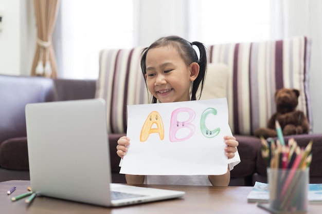 Heureuse petite fille asiatique montrer l'apprentissage des devoirs à l'aide d'un ordinateur portable Internet virtuel en ligne étudier à la maison concept d'idée