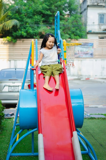 Heureuse petite fille asiatique en robe thaïlandaise jouant dans une aire de jeux pour enfants