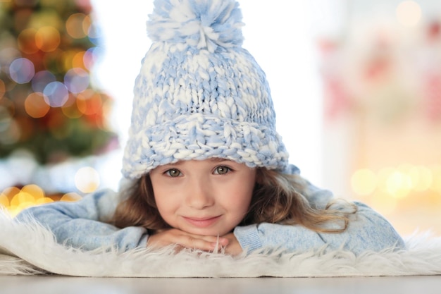 Heureuse petite fille au chapeau allongée sur un tapis à la maison