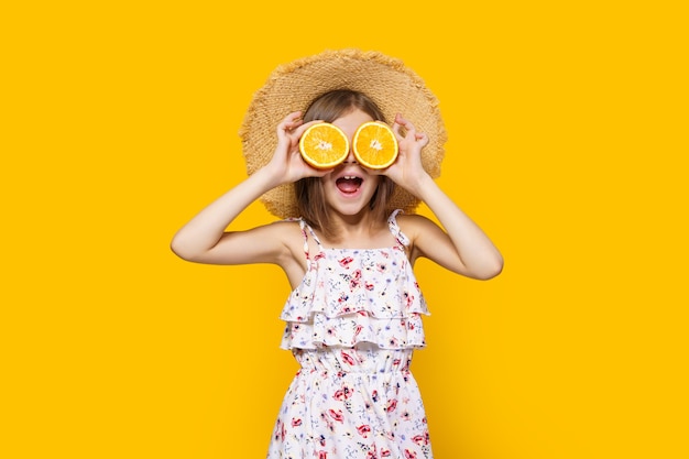 Heureuse petite fille au chapeau de paille tenant une orange sur fond jaune avec un espace réservé au texte