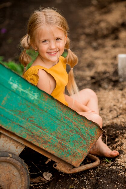 heureuse petite fille blonde à la campagne dans une brouette de jardin assise souriante