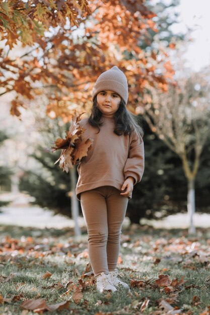 heureuse petite fille brune dans un bonnet tricoté se promène dans le parc en automne