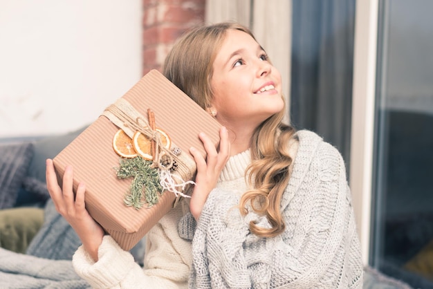 Photo heureuse petite fille avec un cadeau dans les mains rêvant