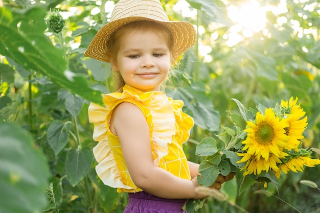 heureuse petite fille en chapeau de paille jouant dans un champ de tournesol en fleurs aux beaux jours d'été