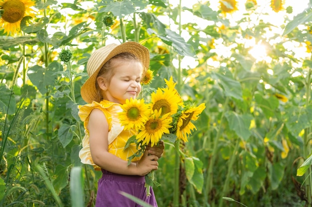 heureuse petite fille en chapeau de paille jouant dans un champ de tournesol en fleurs aux beaux jours d'été