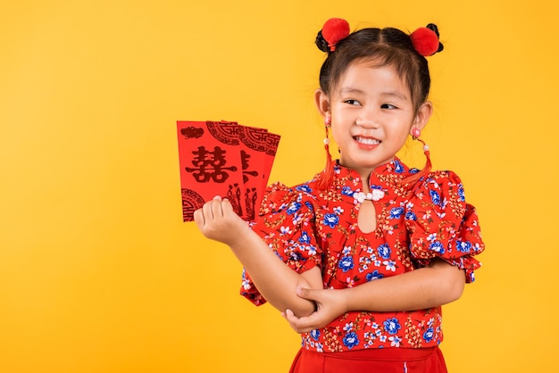 Heureuse petite fille chinoise asiatique sourire porter cheongsam rouge qipao tenir angpao paquet rouge cadeau monétaire