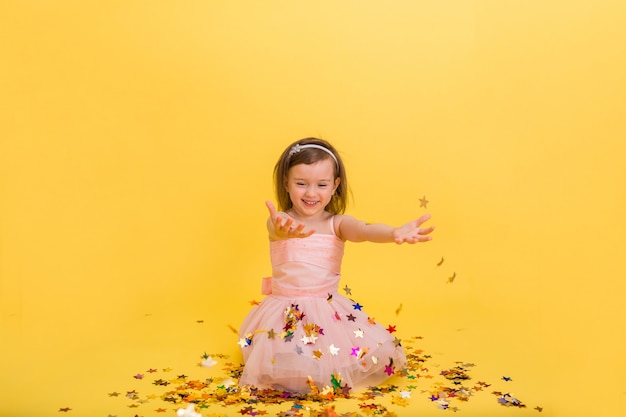 heureuse petite fille dans une robe rose gonflée attrape des confettis avec ses mains sur un jaune isolé