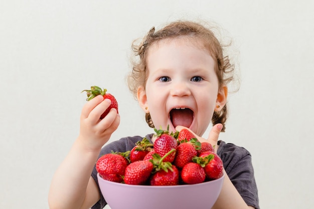 Heureuse petite fille drôle tenant dans la main une fraise sucrée. Vue rapprochée.