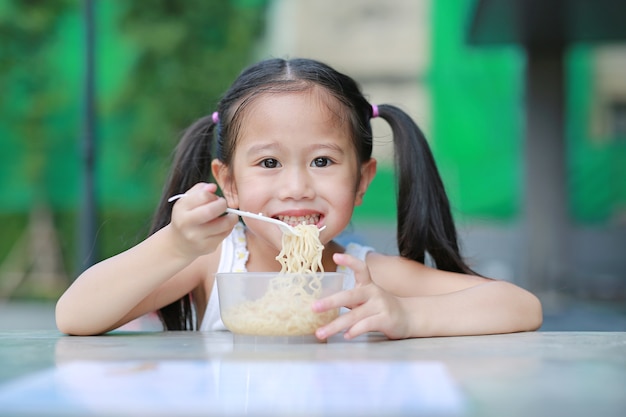 Heureuse petite fille enfant asiatique manger des nouilles instantanées au jardin.