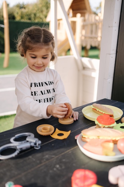 Heureuse petite fille jouant sur la cuisine jouet sur roues jolie fille faire un hamburger sur la cuisine jouet à l'extérieur