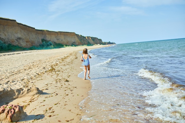 Heureuse petite fille joyeuse courir sur la plage