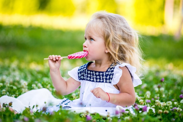 Photo heureuse petite fille mangeant un bonbon sur un bâton en forme de coeur concept de la saint-valentin