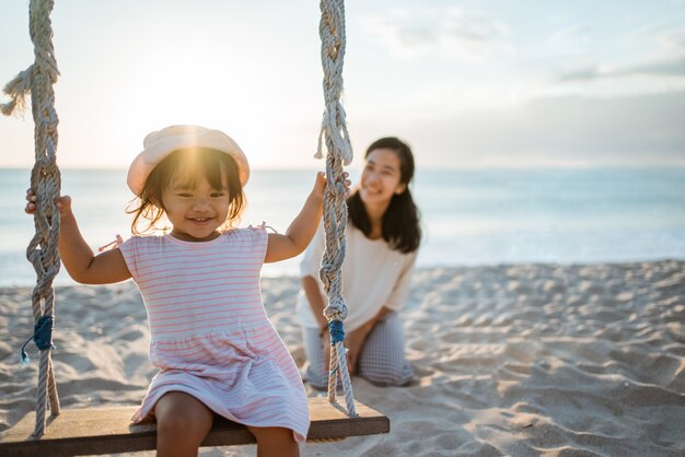 Heureuse petite fille et mère se balançant à la plage