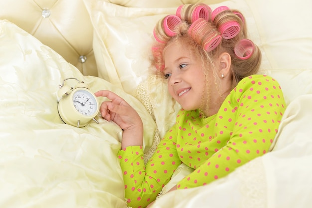 Heureuse petite fille mignonne en bigoudis s'est réveillée avec une horloge