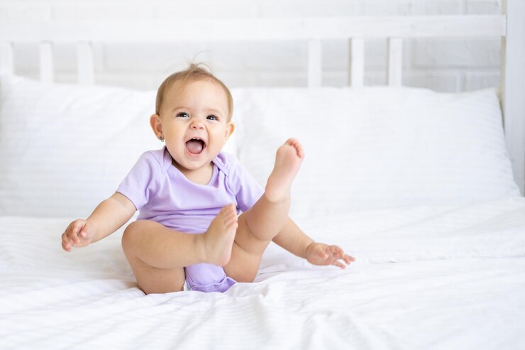 Photo heureuse petite fille mignonne en body est assise sur un lit sur une literie blanche, souriante. le concept de produits pour bébés.
