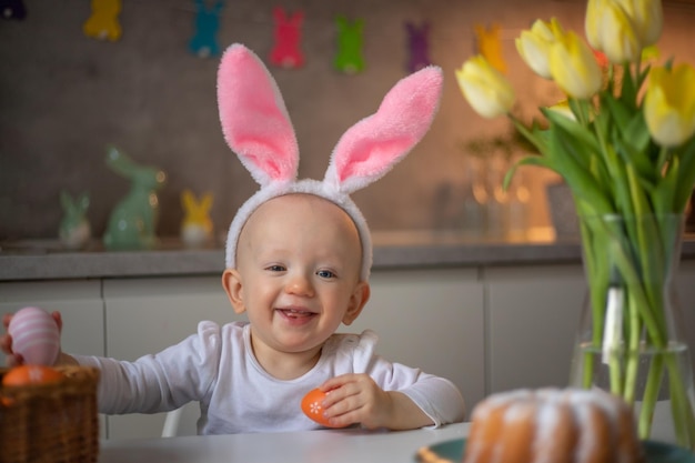 Heureuse petite fille mignonne portant des oreilles de lapin le jour de pâques assis à la table dans la cuisine